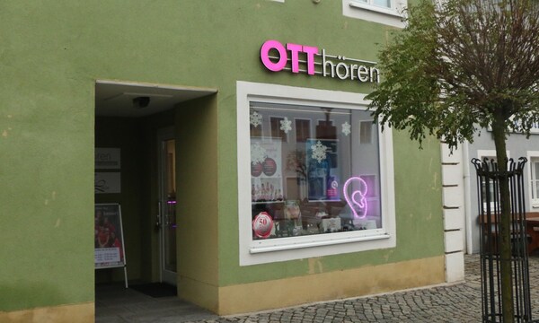 Fassade eines Hörakustikgeschäfts mit Schaufensterdekoration und leuchtendem Ohr-Symbol.